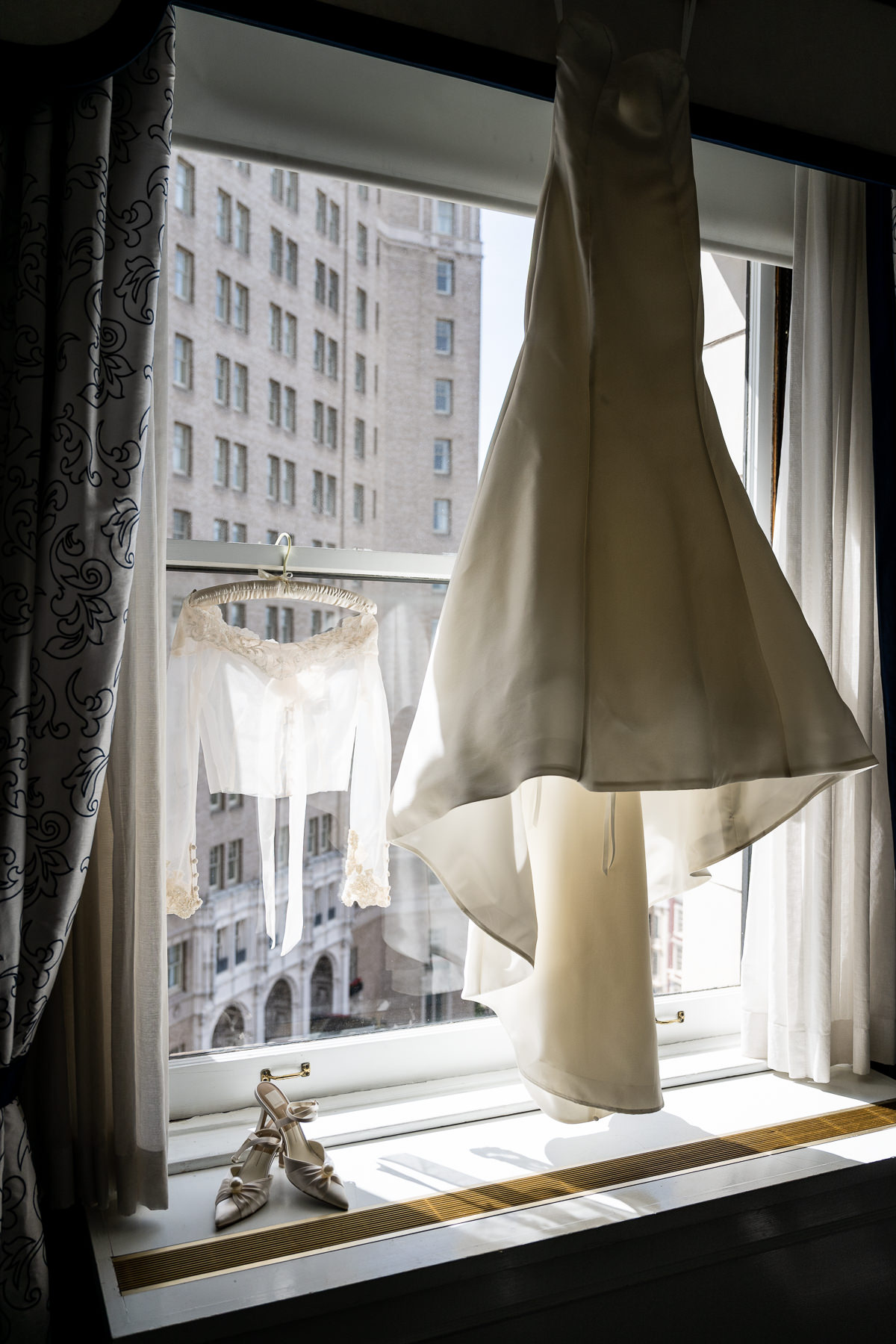 Bridal gown hanging in window with San Francisco skyline backdrop — Adrianne and Connor's Julia Morgan Ballroom wedding