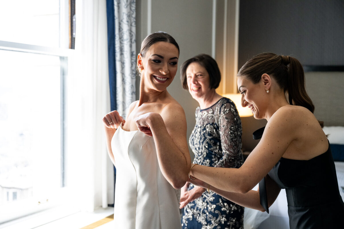 Getting ready photo at the Fairmont Hotel of the bride being helped by her mom and sister. Photo by San Francisco Wedding Photographer Duy Ho