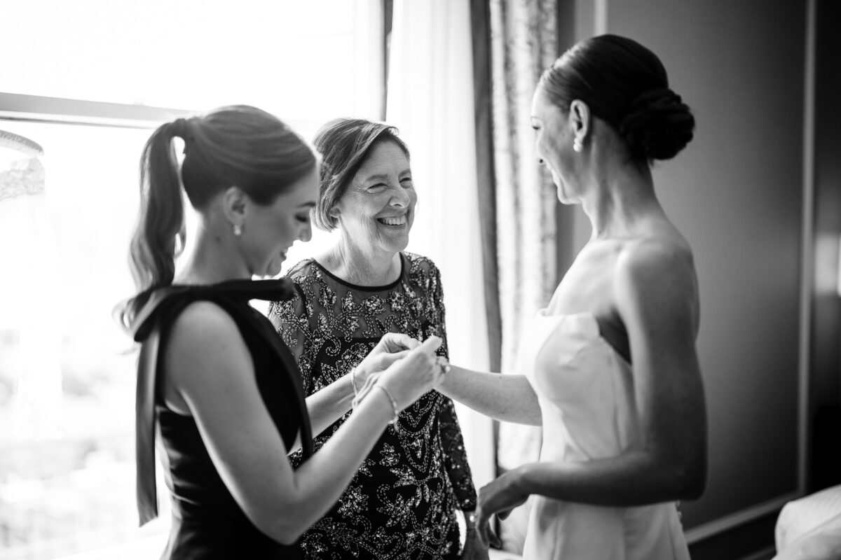 Photo of bride's mom smiling at her daughter while the bride's sister helps with her bracelet at the Fairmont Hotel. Photo by San Francisco Wedding Photographer Duy Ho