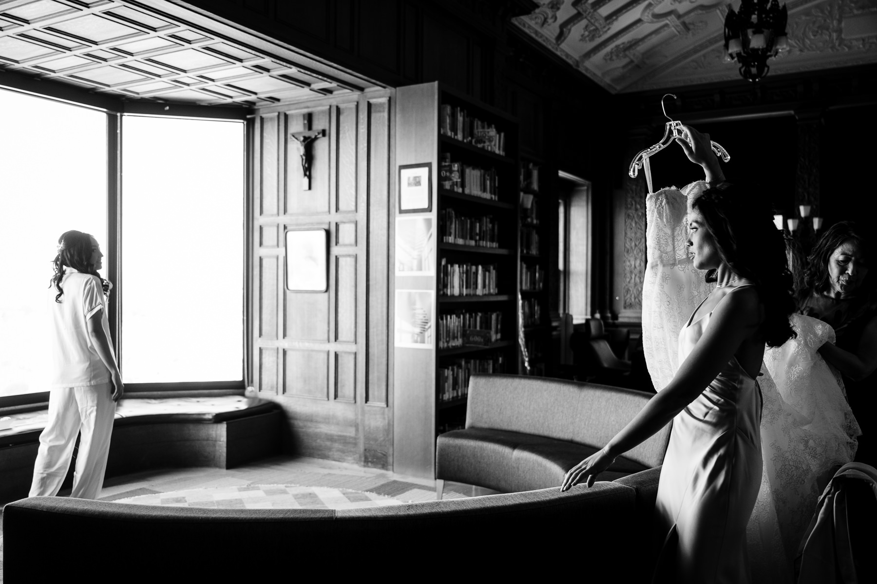 Black and white photo of bride getting dressed in Flood Mansion library with bridesmaid helping, bay window light