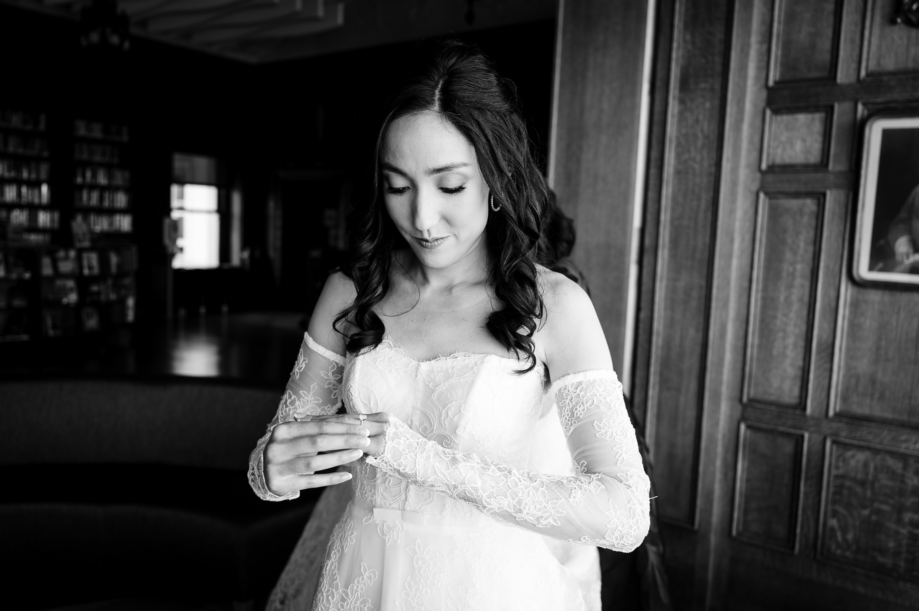 Black and white portrait of bride in full lace gown standing in Flood Mansion library before ceremony