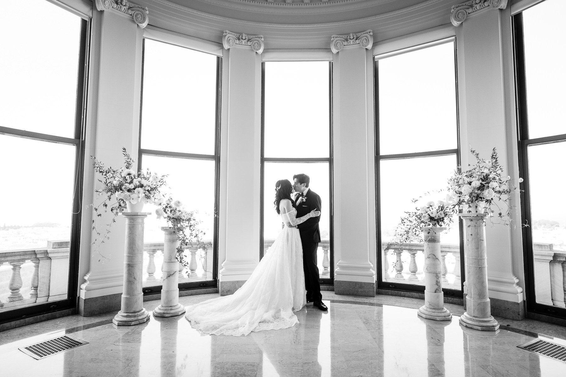 Bride and groom kissing in front of Grand Hall bay windows with white floral columns, Flood Mansion ceremony portrait