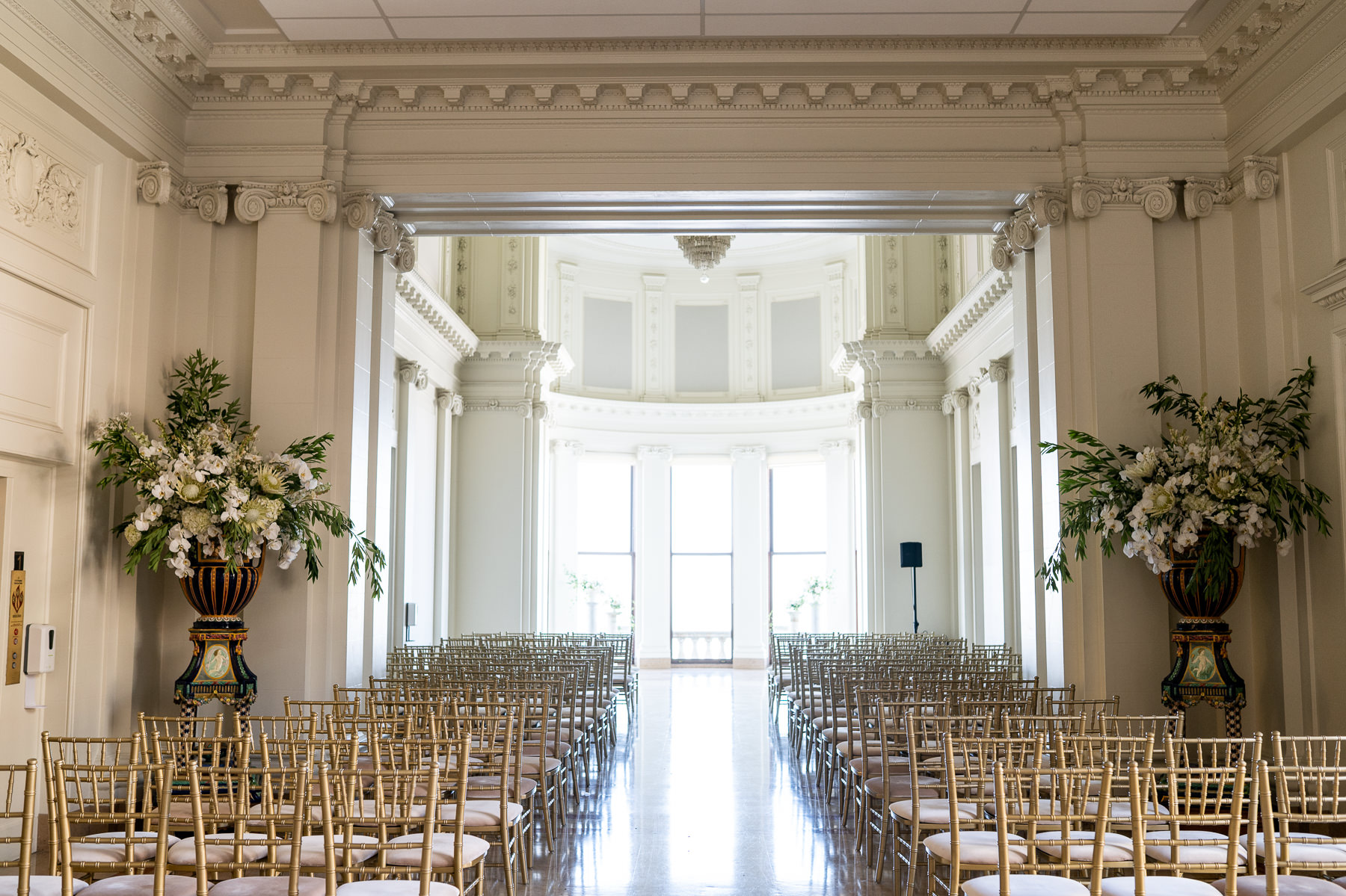 Grand Hall ceremony setup at Flood Mansion — gold chiavari chairs, white floral arrangements, bay windows, San Francisco