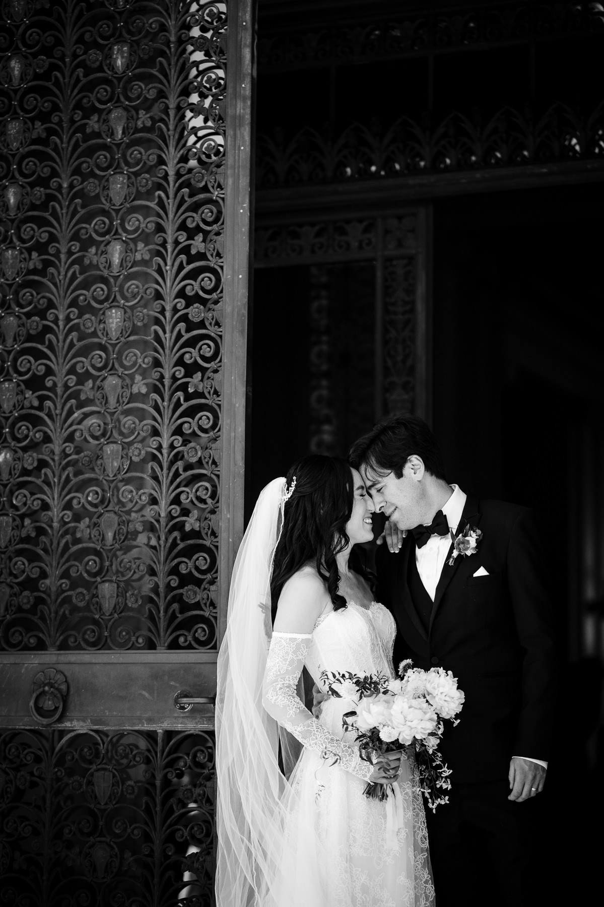 Black and white portrait of couple outside Flood Mansion arched iron gate, bride in lace gown, San Francisco