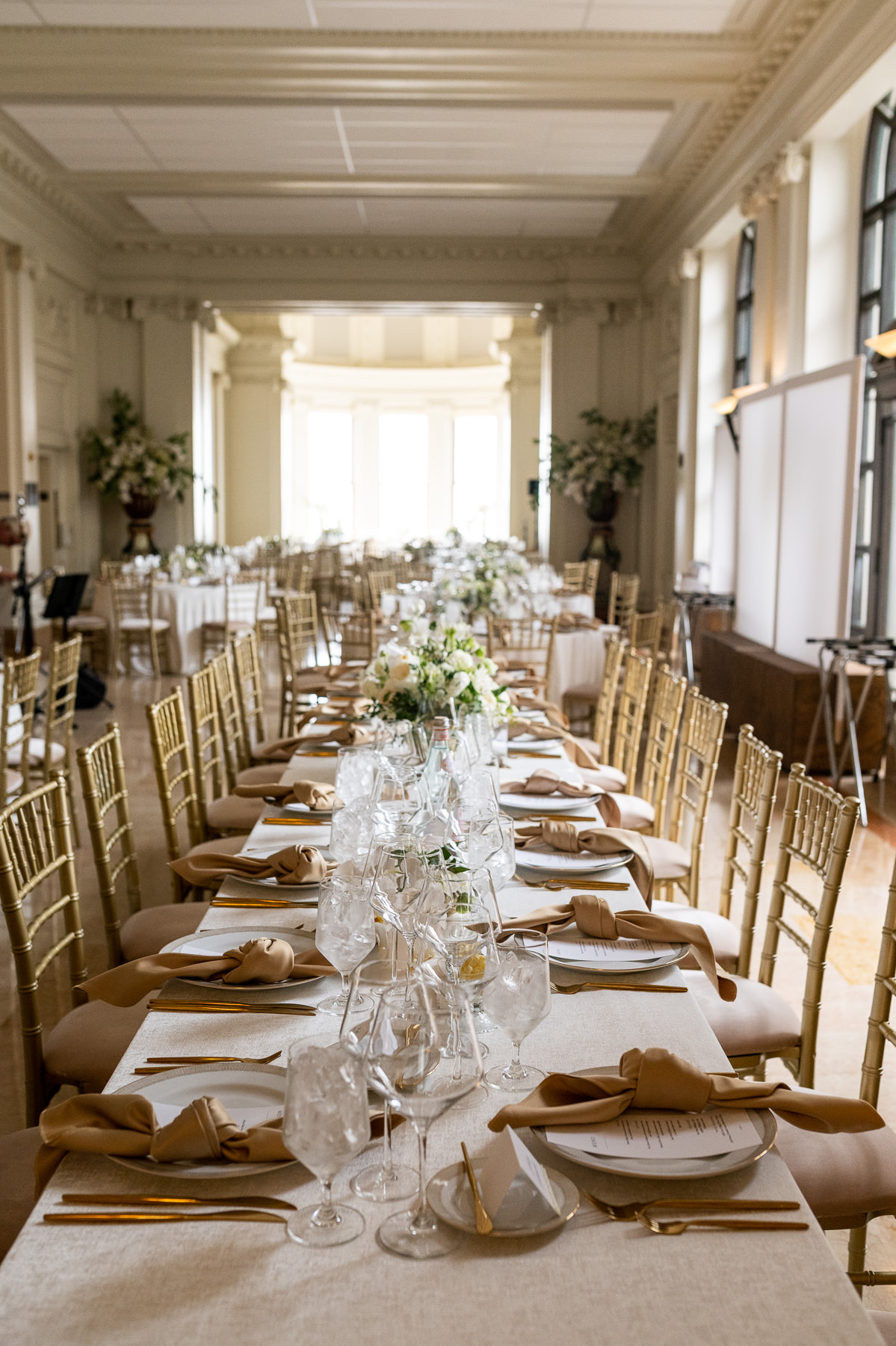 White wedding cake with greenery displayed against ornate white plaster wall at Flood Mansion reception, San Francisco