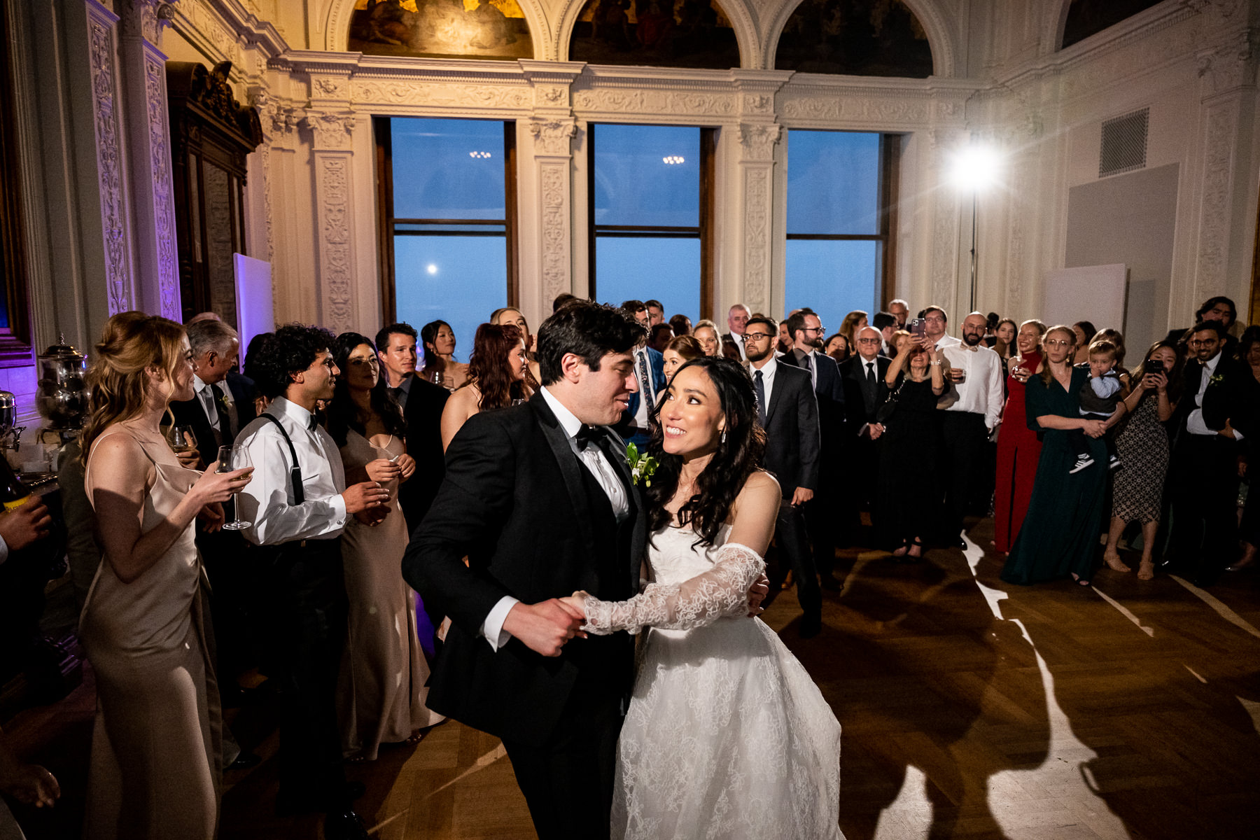 Black and white photo of bride and groom cutting wedding cake at ornate Flood Mansion plaster wall, laughing together